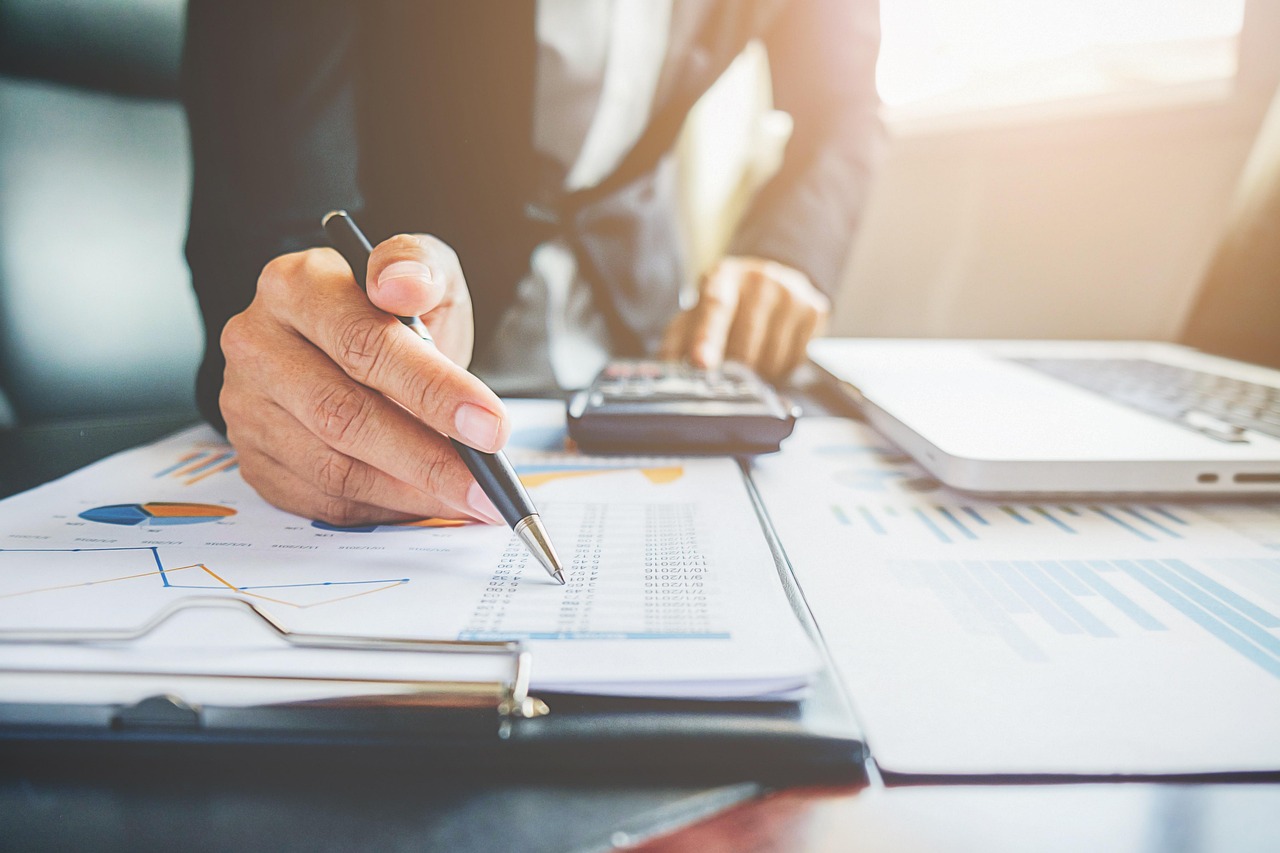 Business person in suit using a pen to review financial charts and data next to a calculator and laptop.